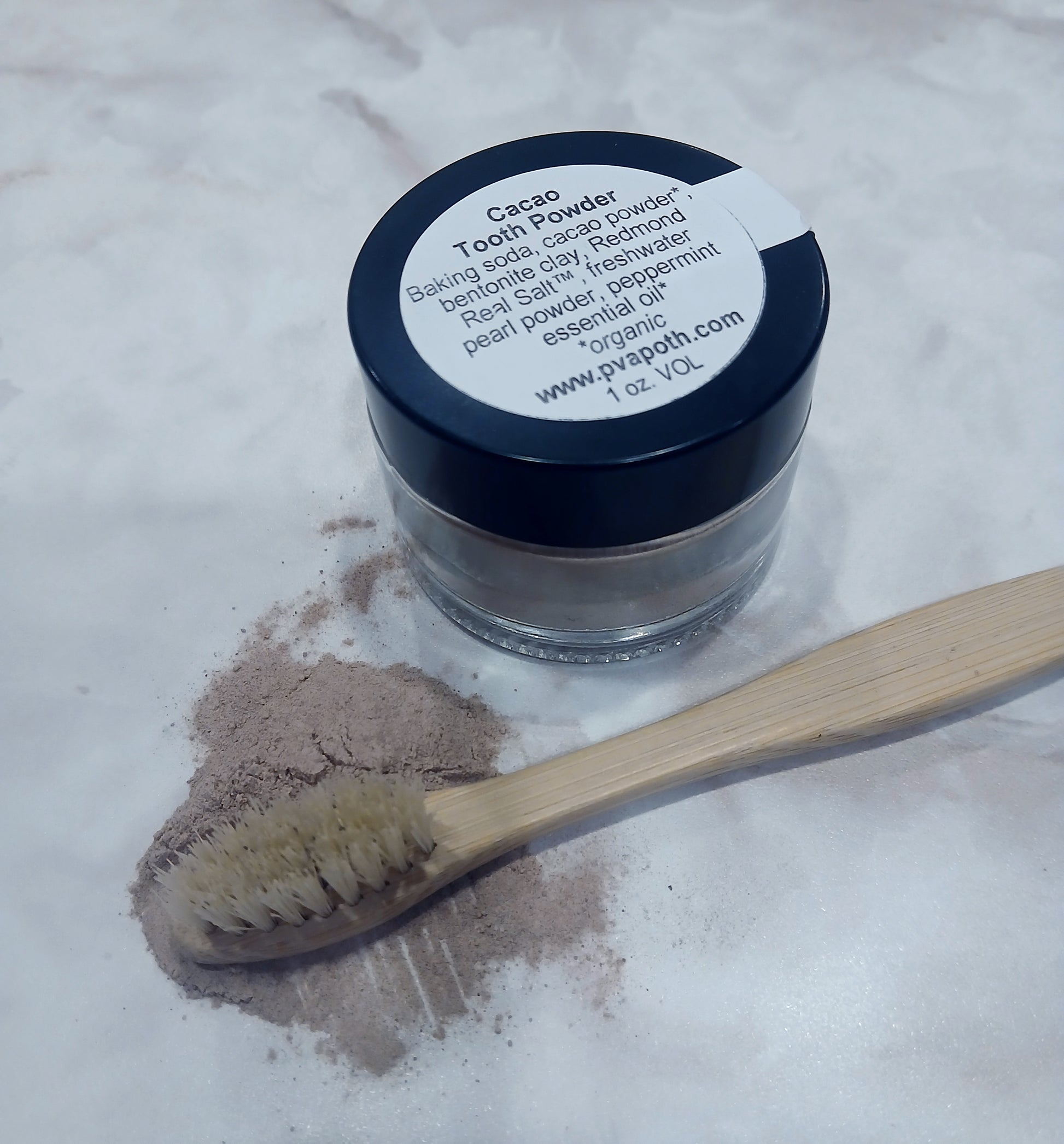 picture of 1 ounce jar of cacao tooth powder some spilled out beside it and a bamboo, boars hair bristle toothbrush laying beside it